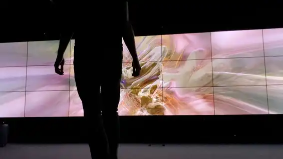 A photo of SELF ABSORBED, an interactive installation by Tim Murray-Browne. A man stands in front of a video wall showing an abstract image rendered in real-time in response to the man's movements.