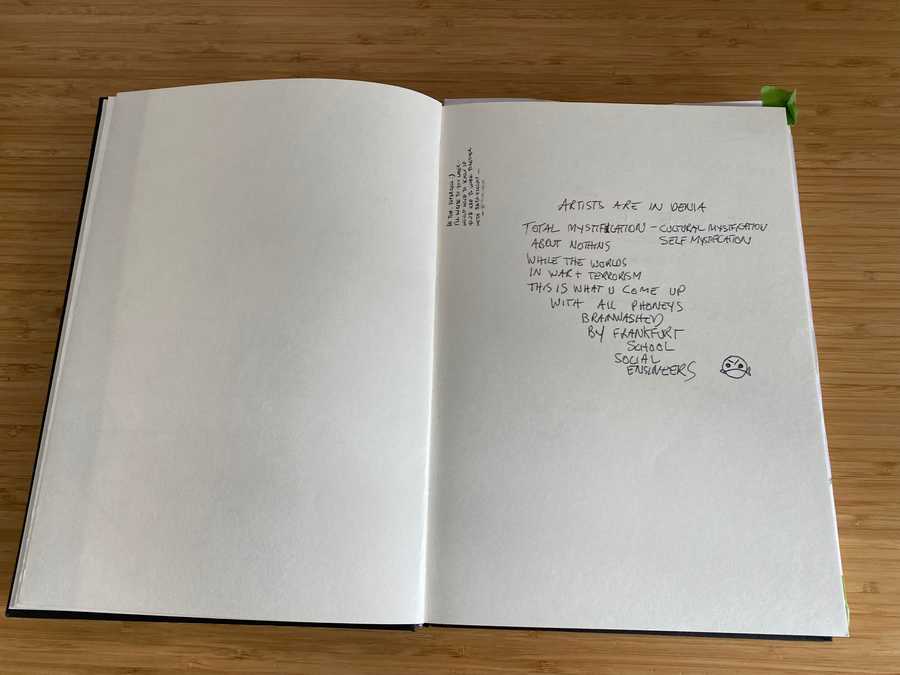 Photo of a comment book from an exhibition with mostly white space and a dominant negative comment that begins "ARTISTS ARE IN DENIA TOTAL MYSTIFICATIOn - CULTURE MYSTIFCATION SELF MYSTIFICATION ABOUT NOTHING ...".