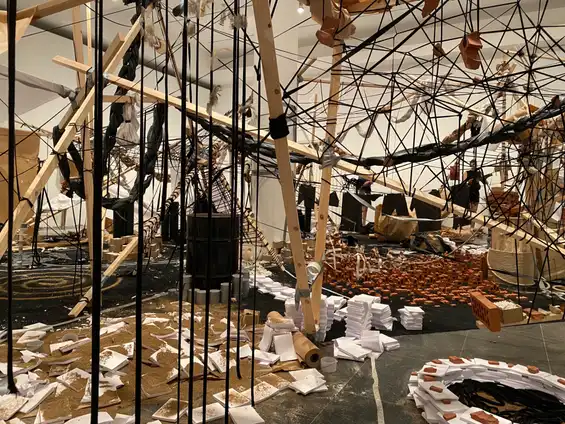 Photo of the first installation at Cinthia Marcelle's exhibition 'A Conjunction of Factors'. It shows a messy array of wood, rope, bricks, tiles, dirt and gaffa tape strung up around the room. Photo by Tim Murray-Browne.