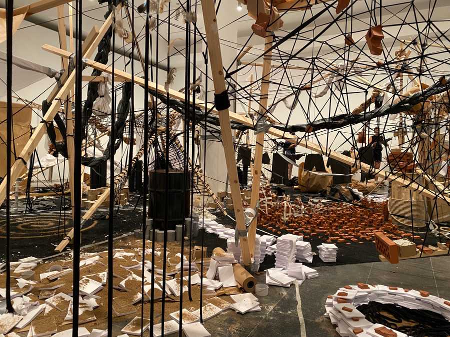Photo of the first room at Cinthia Marcelle's exhibition 'A Conjunction of Factors'. It shows a messy array of wood, rope, bricks, tiles, dirt and gaffa tape strung up around the room. Photo by Tim Murray-Browne.